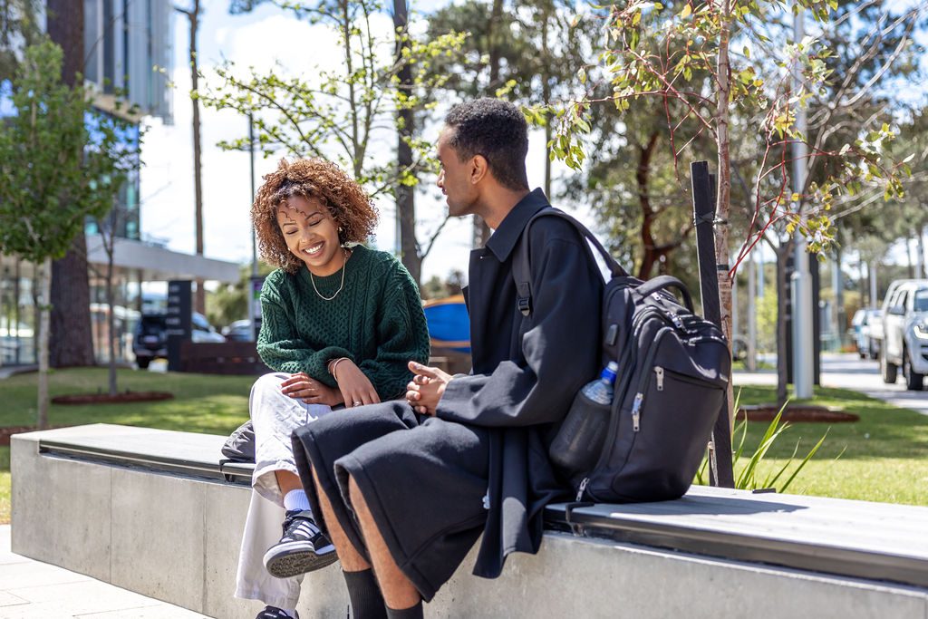 Two Curtin students sitting on the benches outside the design precinct