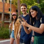 three students walking on campus with a mobile phone