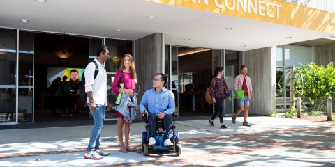 Two students standing next to a man in a wheelchair, outside of Curtin Connect
