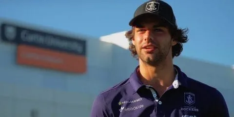 A man in a purple shirt, standing in front of the Curtin Stadium