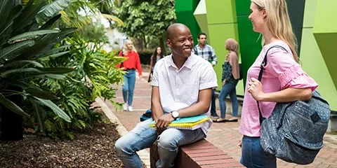 Two students sitting on a brick wall talking