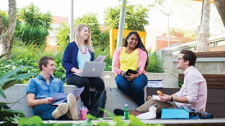Group of four students smiling while sitting outside together