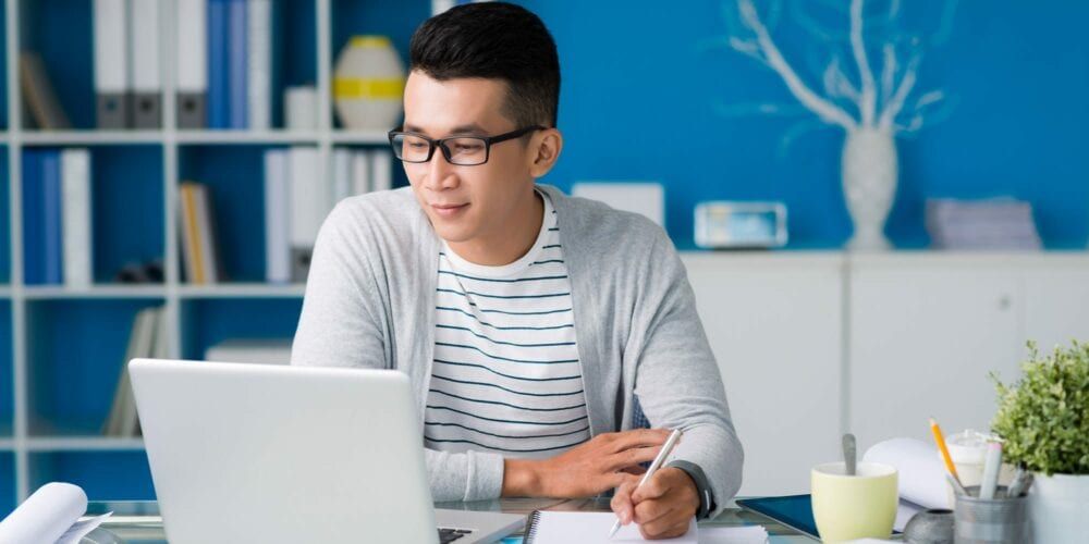 Student learning from home using laptop and taking notes