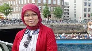 Curtin postgraduate student Netty Muharni wearing a red headscarf, standing on a bridge, with a scenic view in the background.