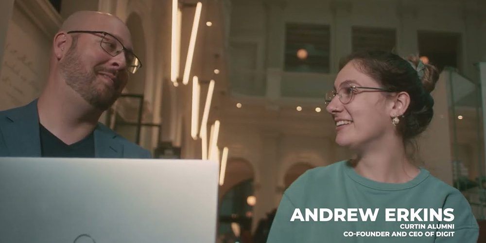 Two students in front of a laptop - play video