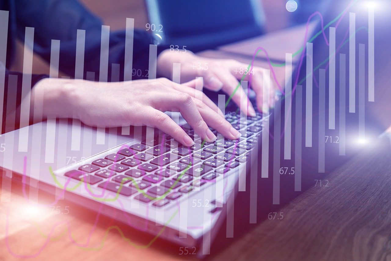 Close up of hands typing on a laptop keyboard overlaid with a transparent statistical bar chart