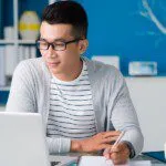 Student learning from home using laptop and taking notes