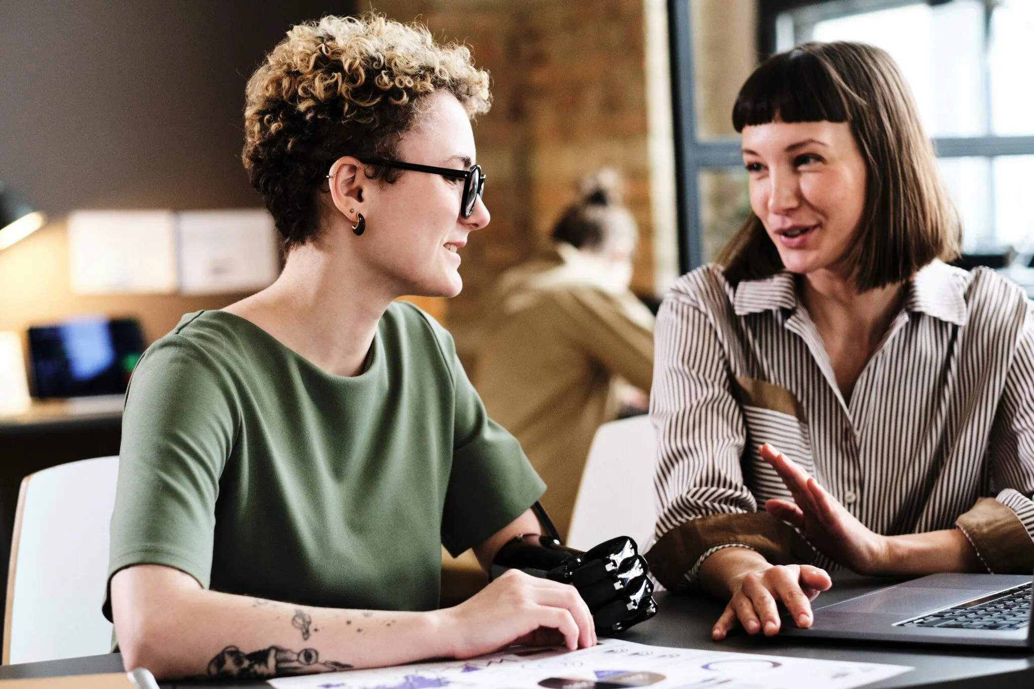 Two people sit at an office desk together, one with a prosthetic arm