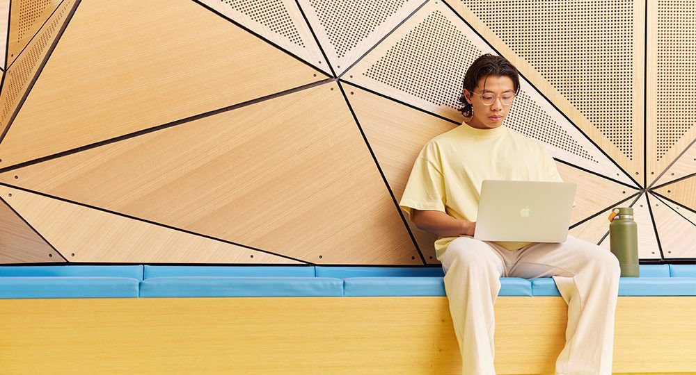 Student studying with a laptop, sitting on a bench in front of an abstract background