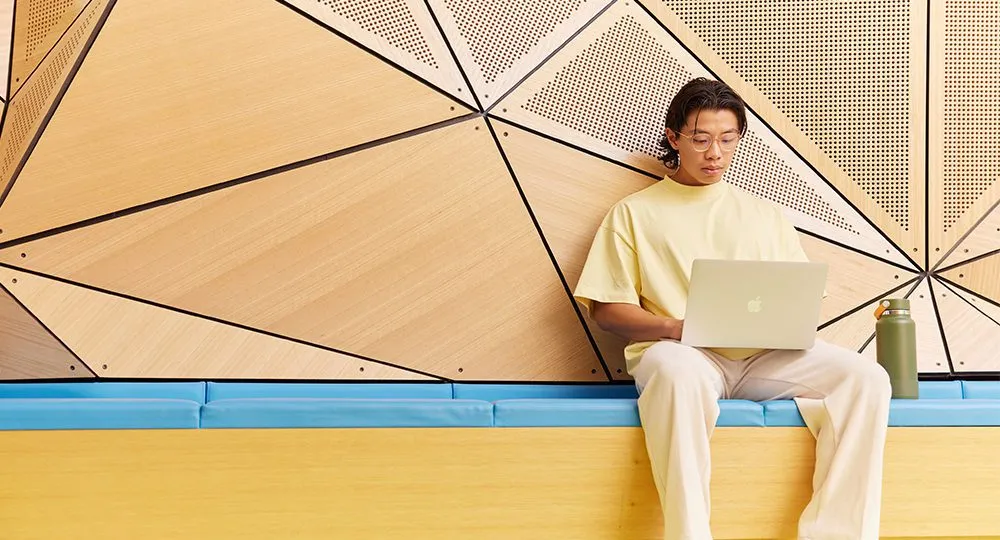 Student studying with a laptop, sitting on a bench in front of an abstract background