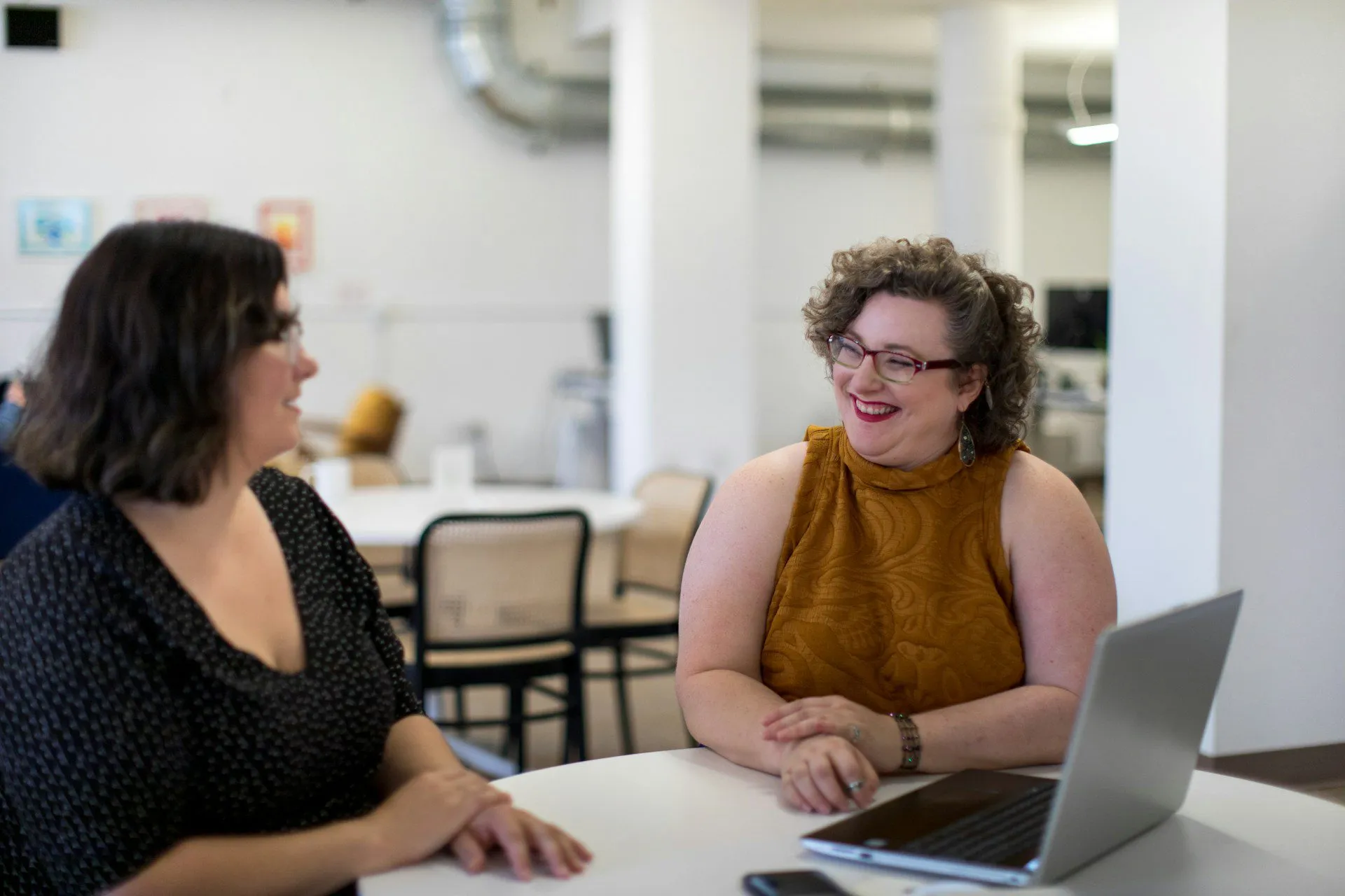 two people sitting at a desk talking with a laptop in front of them