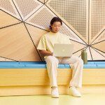 Student studying with a laptop, sitting on a bench in front of an abstract background