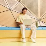 Student studying with a laptop, sitting on a bench in front of an abstract background