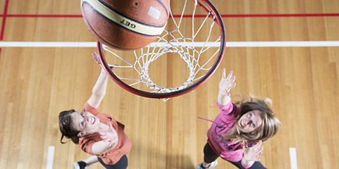 Two female basketball players jumping in the air, trying to catch a basketball