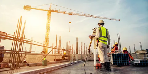 Surveyor builder Engineer with theodolite transit equipment at construction site outdoors during surveying work