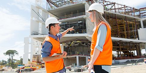 A male and female wearing high-vis standing in front of a building being constructed