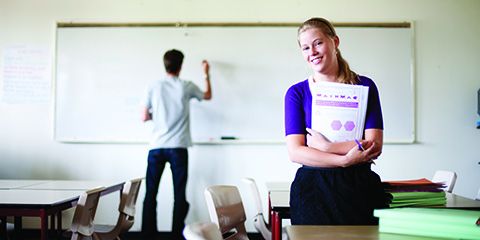 A teacher standing in a classroom writing on a white board