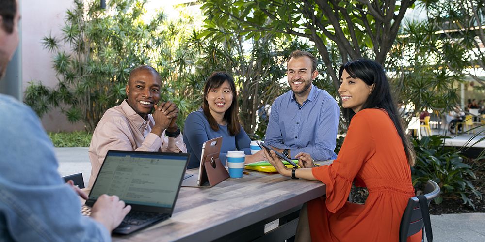 A group of business students, sitting at a table, in front of a laptop, talking to businessman