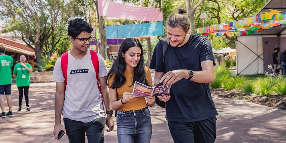 Two male and one female student walking through the Curtin grounds, looking at a brochure