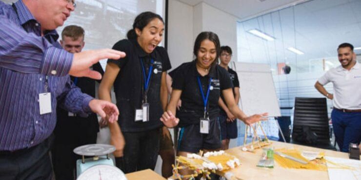 Two female students and some industry members smiling around a table at IAES