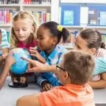 A group of primary school students and a student teacher looking at a globe of the Earth