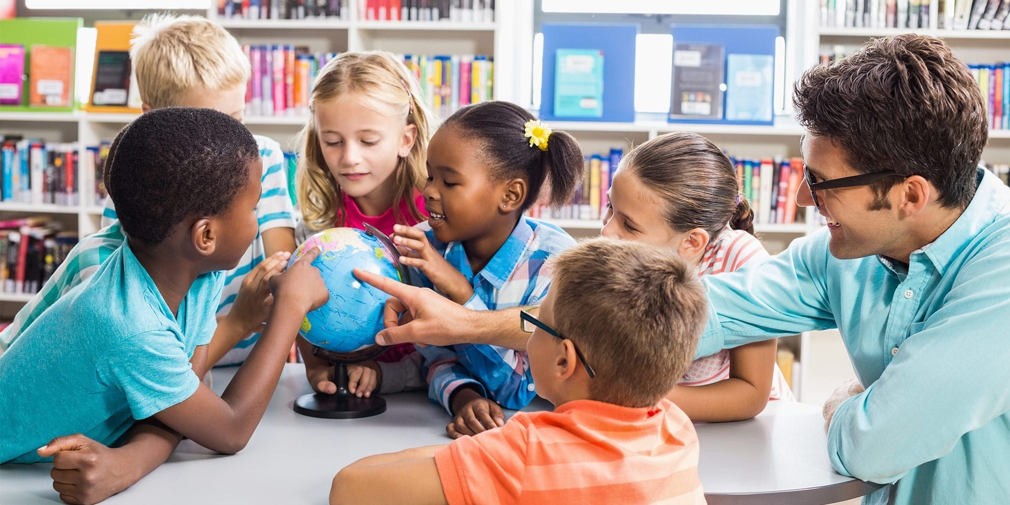 A group of primary school students and a student teacher looking at a globe of the Earth