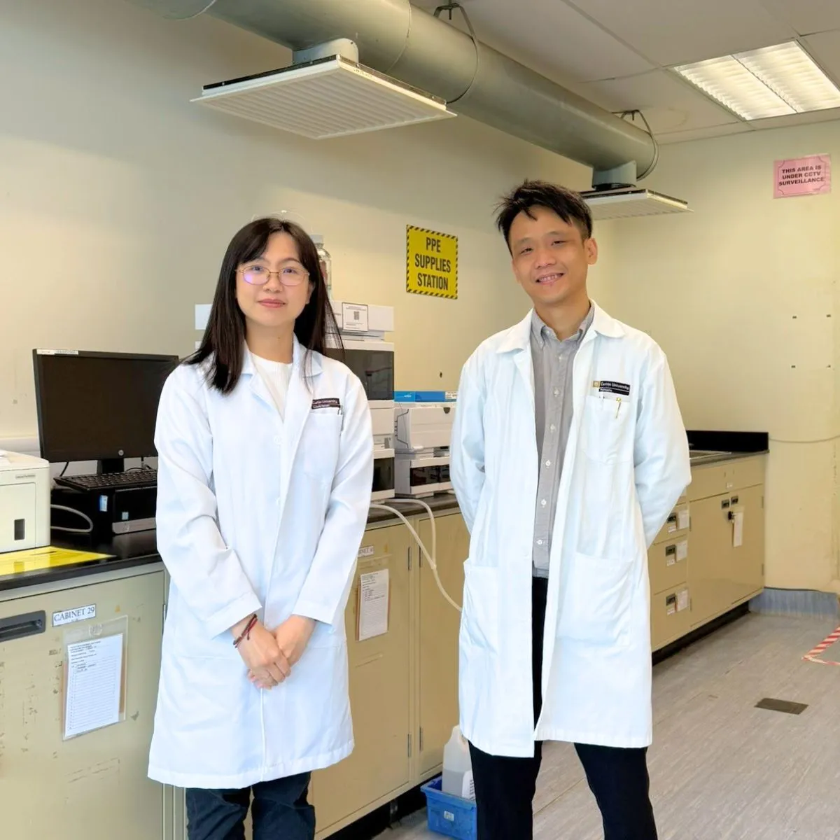 Two people stand in white coats in a laboratory setting.