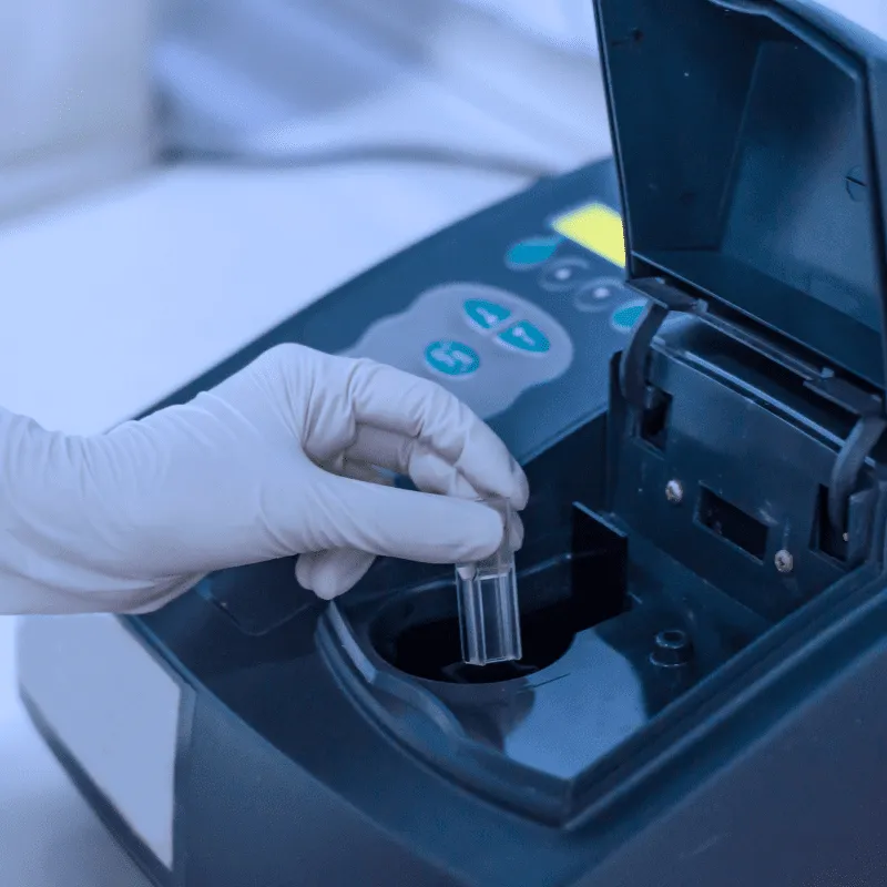 A gloved hand puts a specimen into a spectrophotometer machine to determine bacterial growth by the optical density