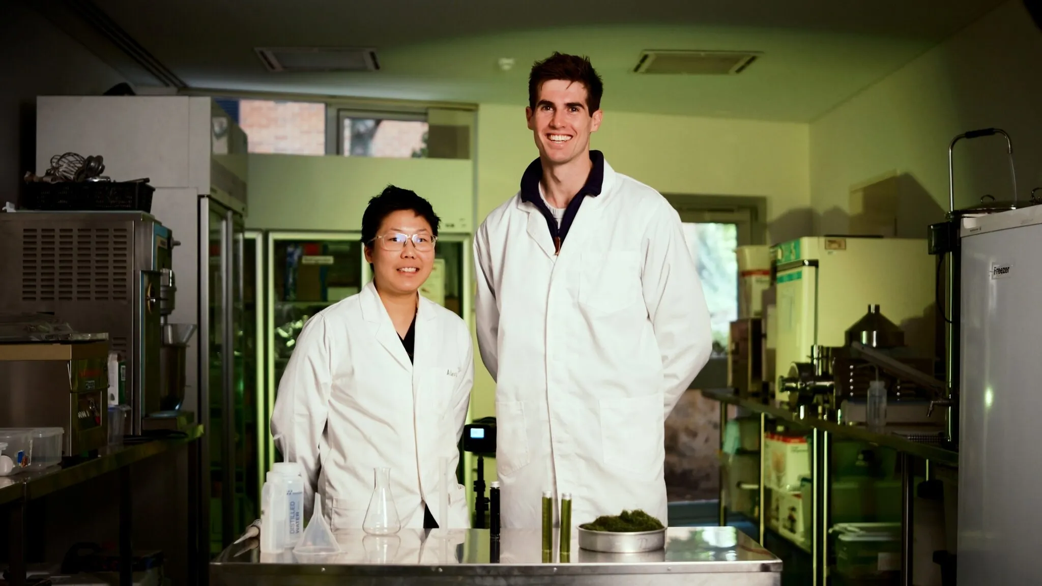 Two Organic Oceans project team members in lab coats working in a laboratory with scientific equipment and seaweed-based substances on the table