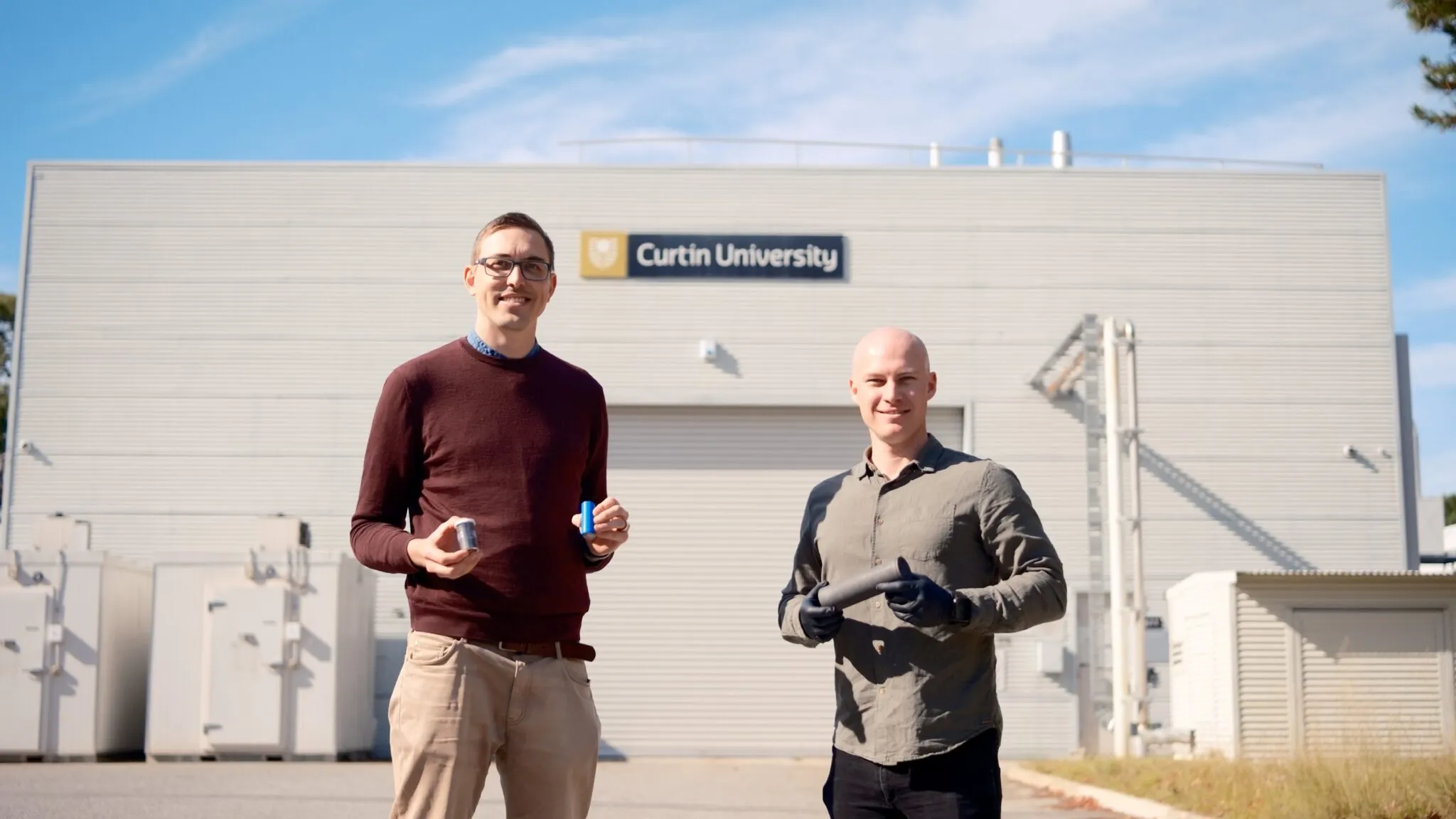 Two RapidGraphite project team members standing outside Curtin University, holding equipment near industrial units.