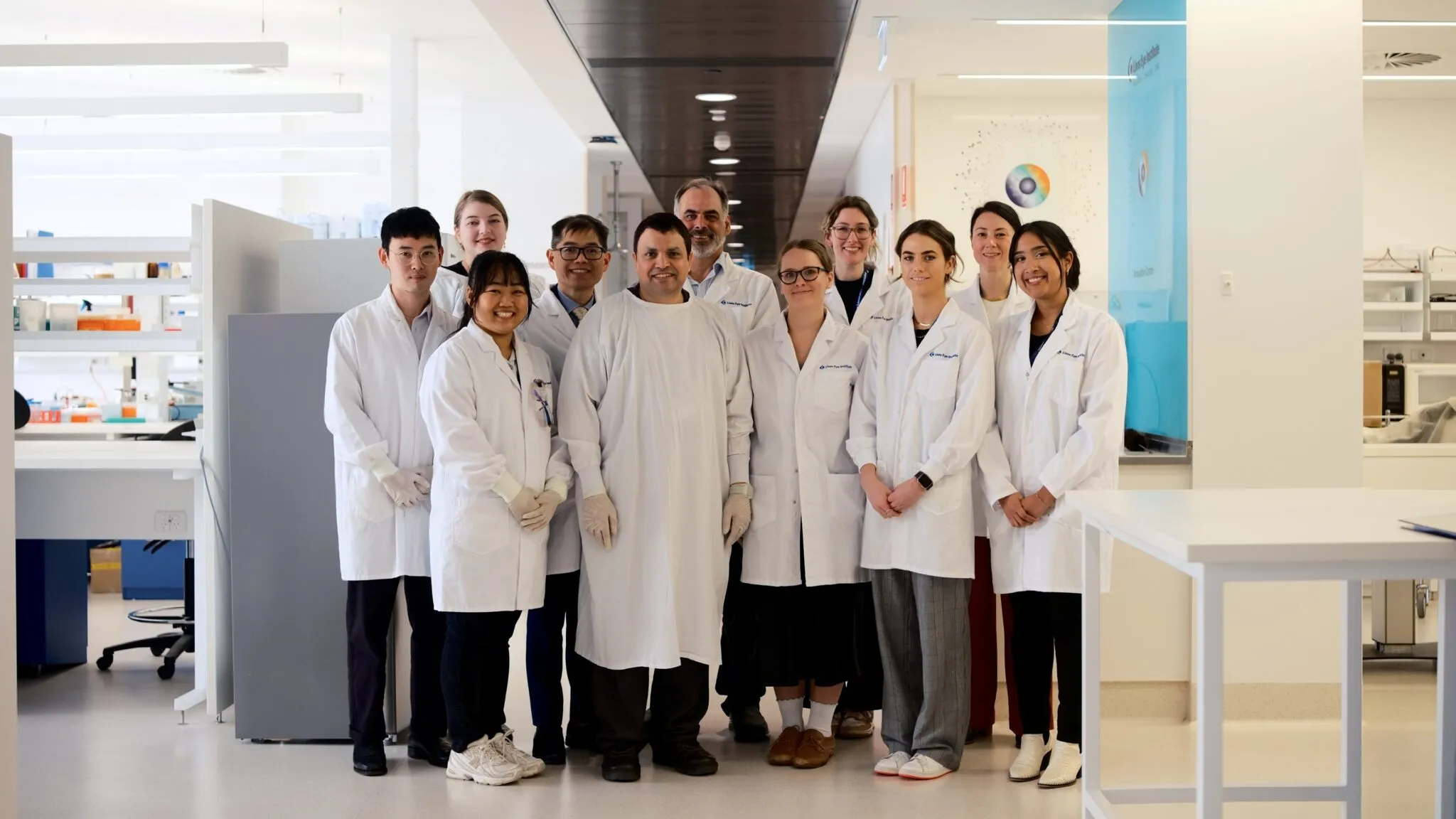 Eleven RetiDrop project team members in white lab coats standing in a laboratory with scientific equipment and workstations.