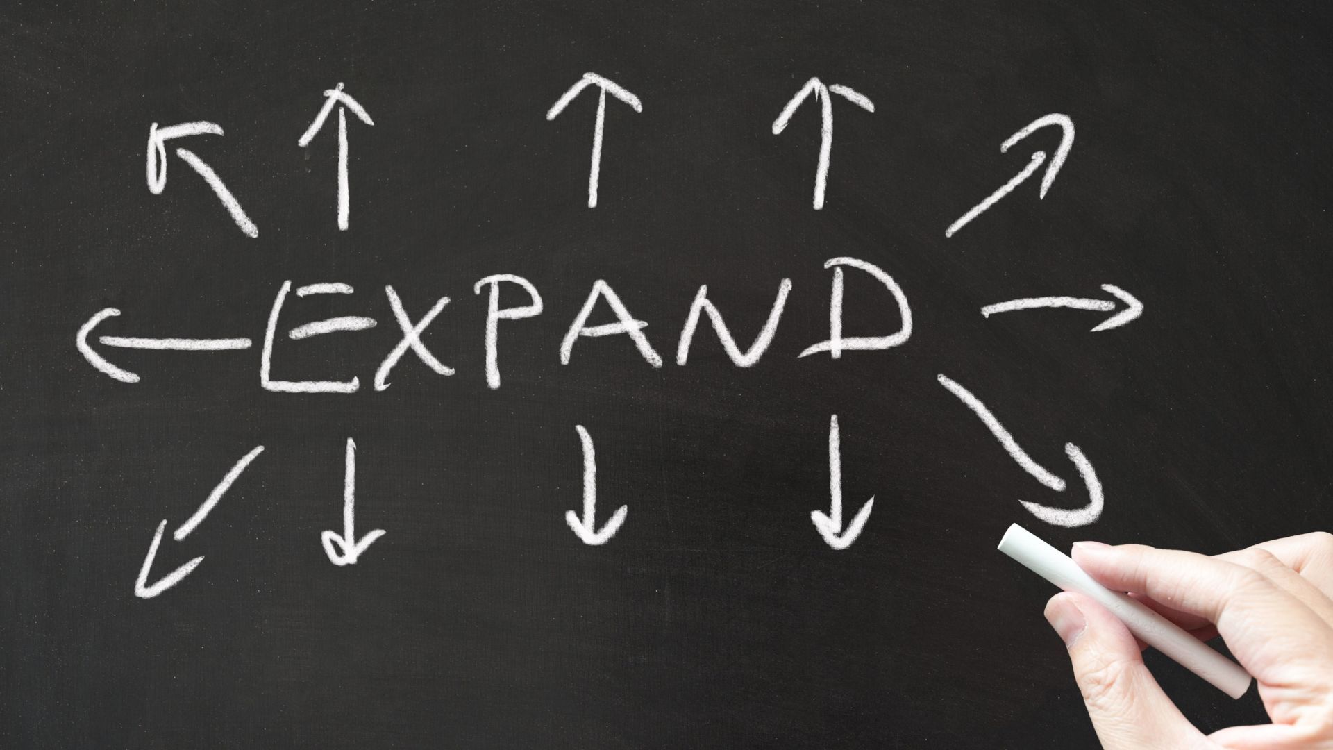 The word “EXPAND” written on a chalkboard with arrows pointing outward in multiple directions, representing growth and expansion.