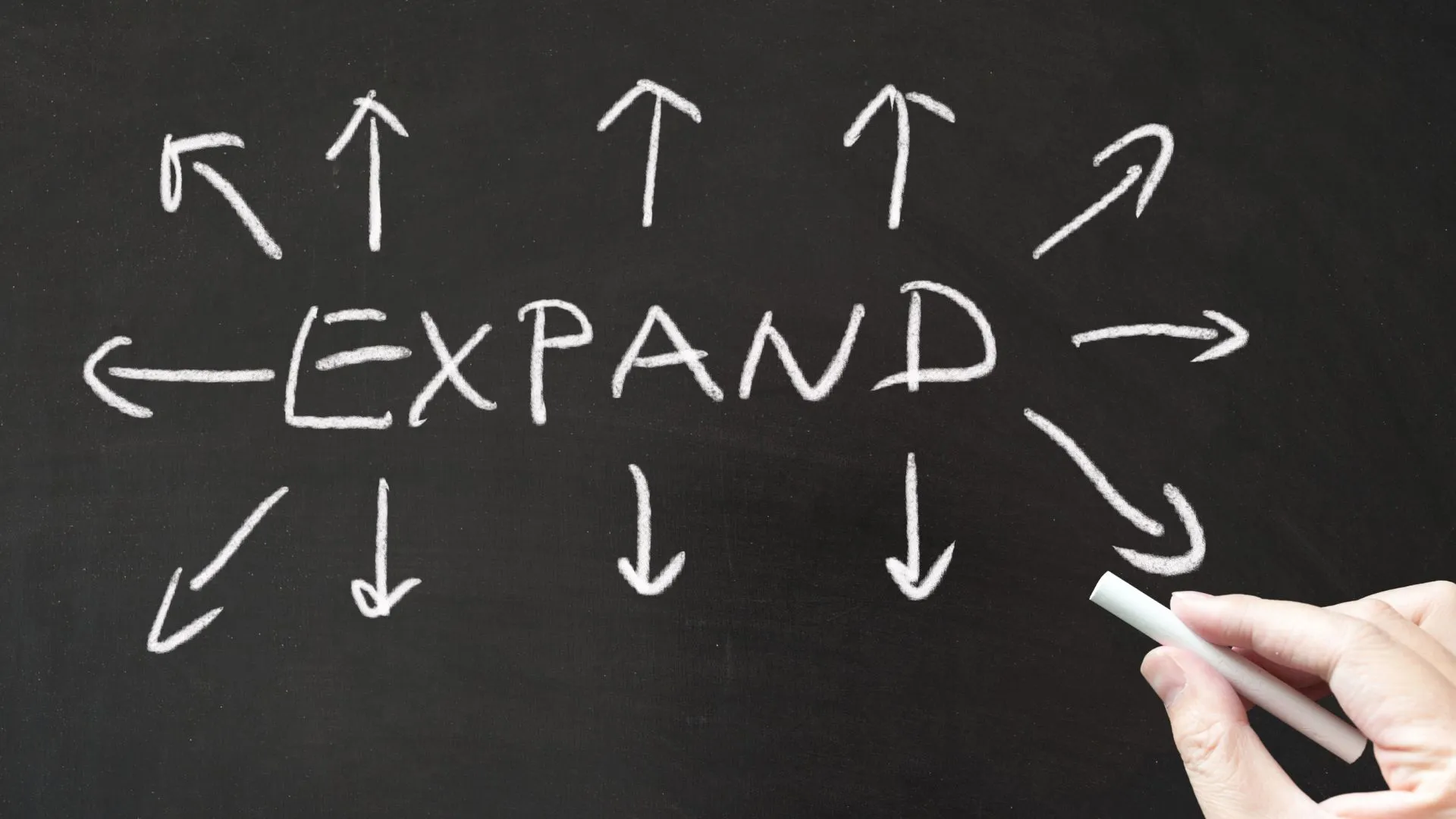 The word “EXPAND” written on a chalkboard with arrows pointing outward in multiple directions, representing growth and expansion.