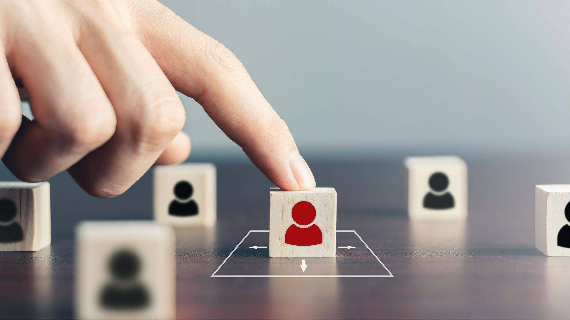 A hand selecting a red human icon among neutral figures, illustrating audience targeting or choosing a specific individual or group.