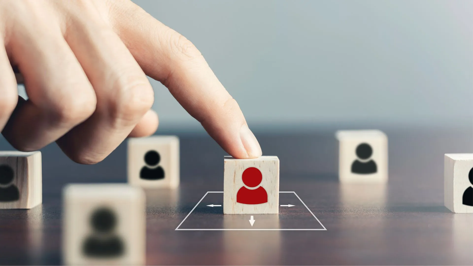 A hand selecting a red human icon among neutral figures, illustrating audience targeting or choosing a specific individual or group.