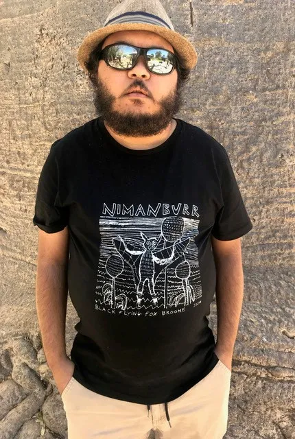 Man in a hat and sunglasses wearing a black t-shirt with graphics on it.