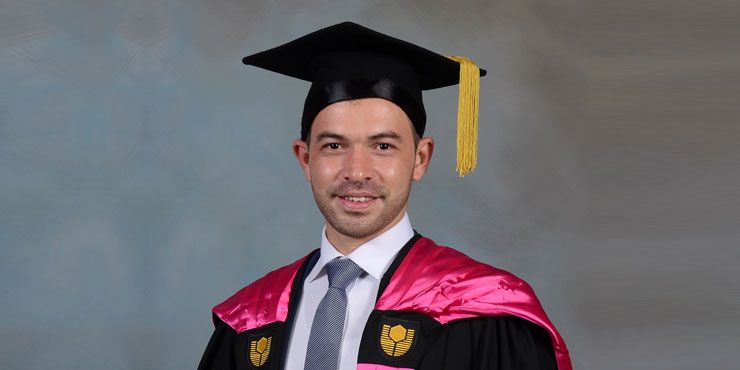 Man in Curtin graduation robes smiling