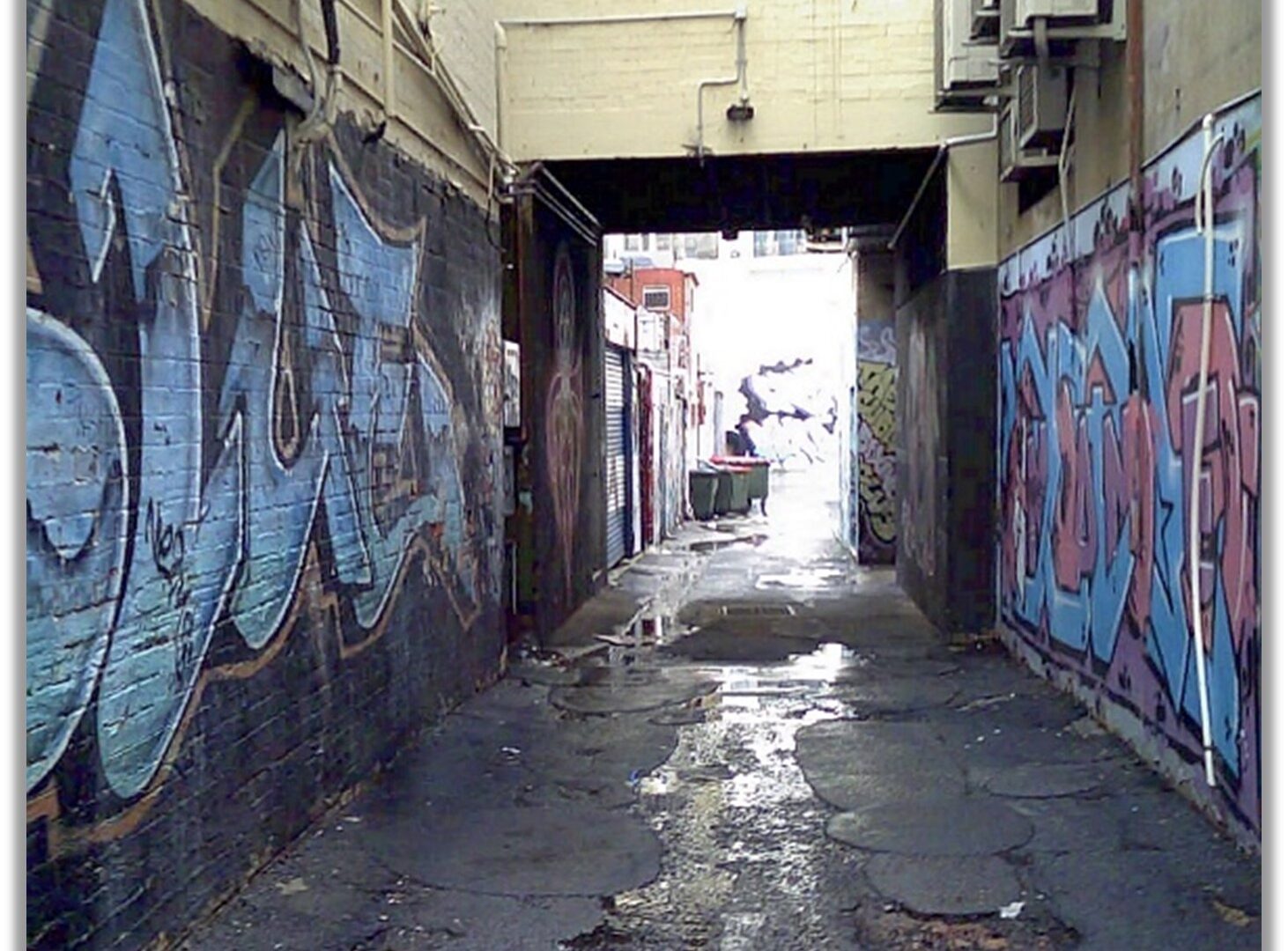 Image of Laneway with puddle on ground and graffit on walls.