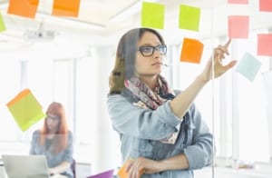 woman sorting through post it notes on a glass wall