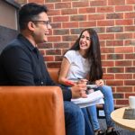 A male and female student sitting on a couch and laughing