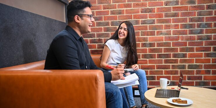 A male and female student sitting on a couch and laughing