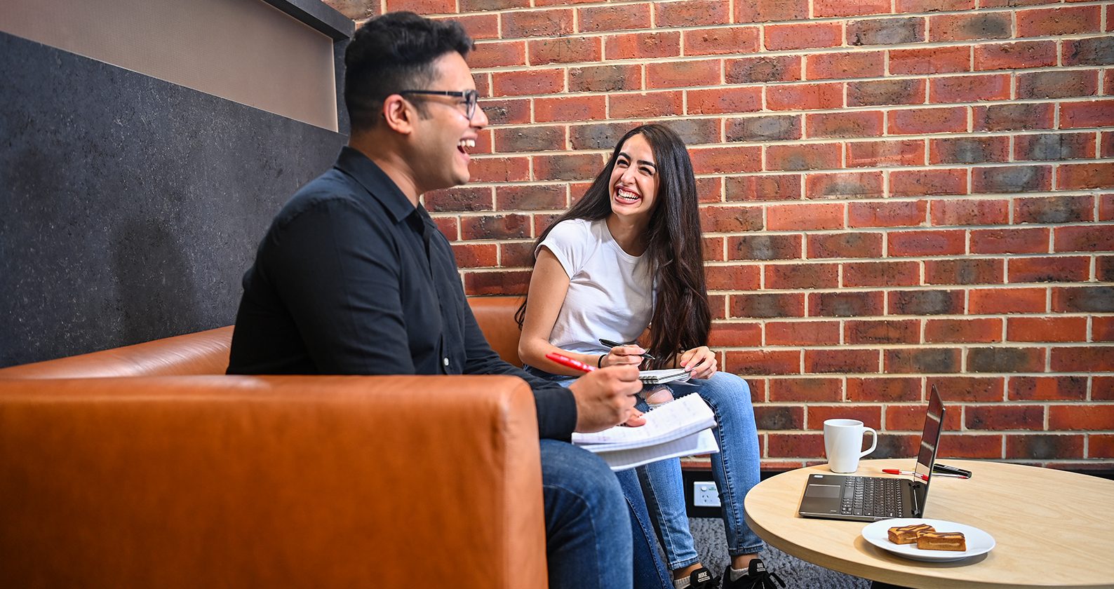 A male and female student sitting on a couch and laughing