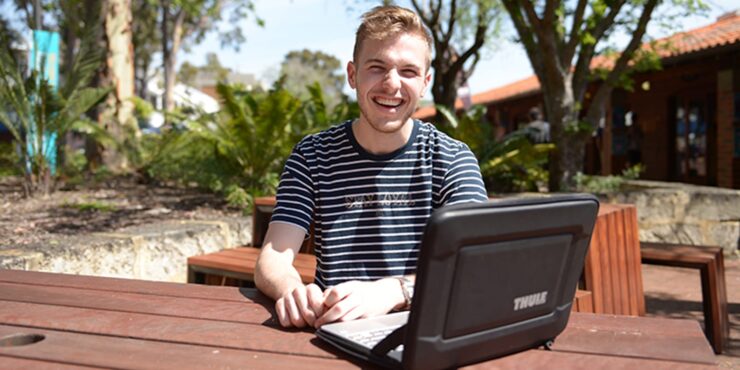 Student sitting outdoors with a laptop.