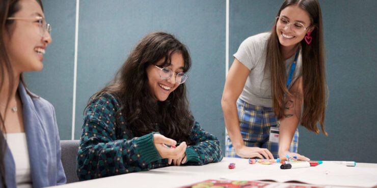 Students at a UniPASS session. Two students are sitting down at a table and the faciliator is standing nearby.
