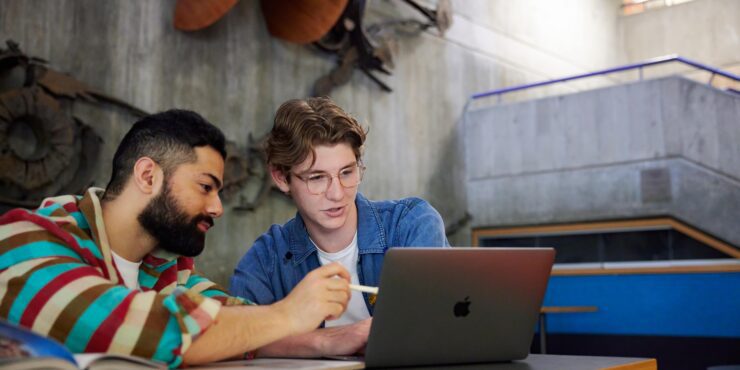 2 students sitting together, looking at a laptop.