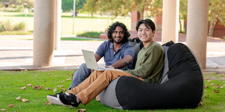 Two students from culturally diverse backgrounds sit together with a laptop
