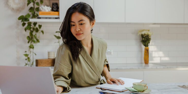 A student leaning against a bench and browsing her laptop.