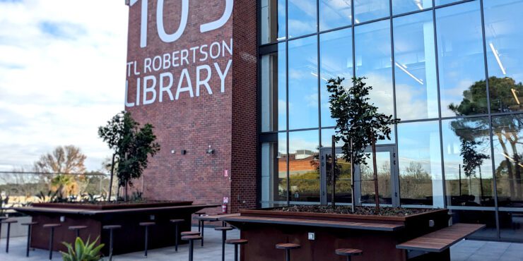 Level 4 outdoor terrace. Wooden benches, some trees and the TL Robertson Library sign is visible on the side of the building.