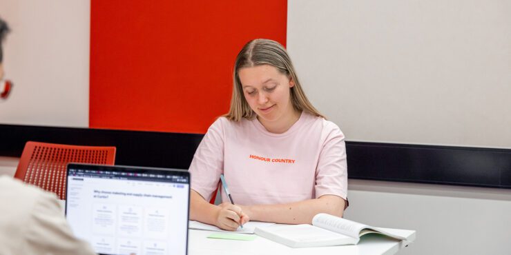 A student writes in her notebook with a textbook open.