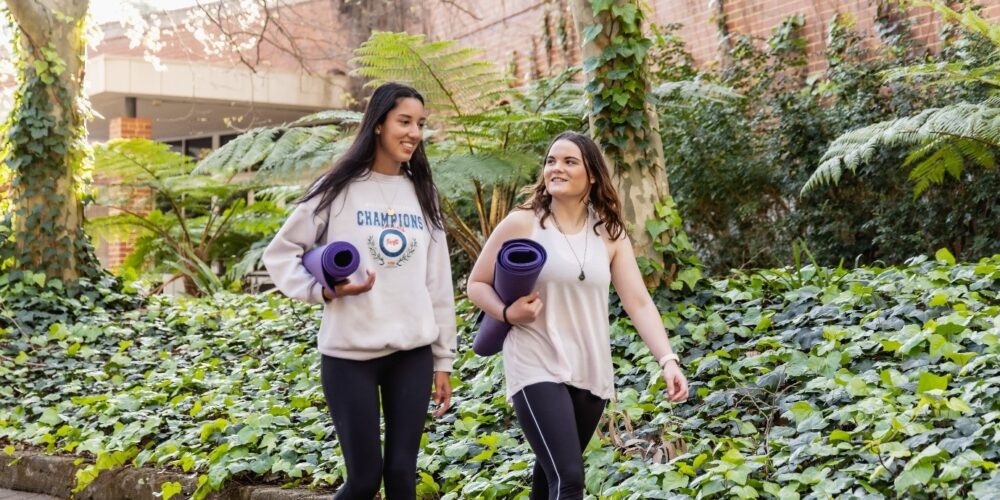 Two students holding yoga mats walking outdoors. 